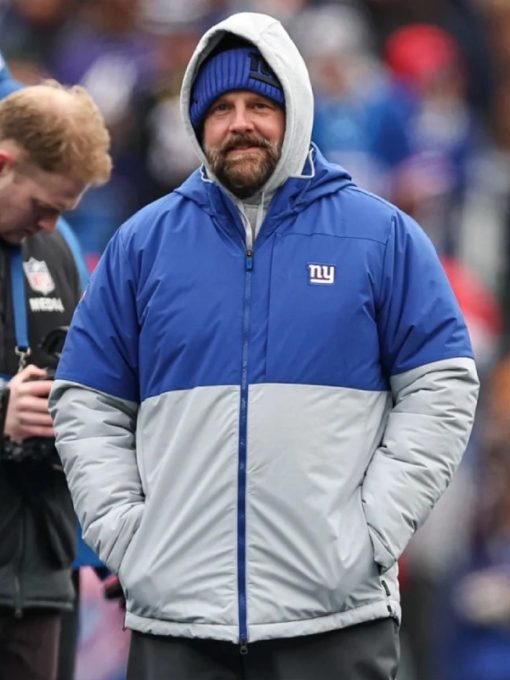 Person wearing a blue and gray jacket with a logo, standing outdoors.