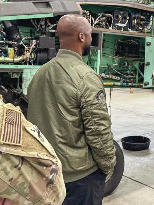 Person wearing a green jacket with a patch in front of an aircraft engine.