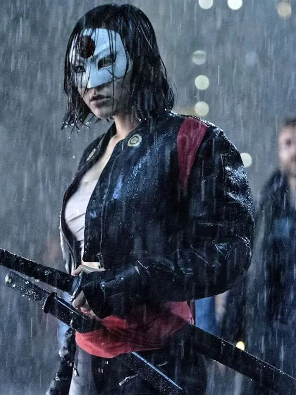 Person in a dark raincoat with a mask holding a weapon, standing in the rain.