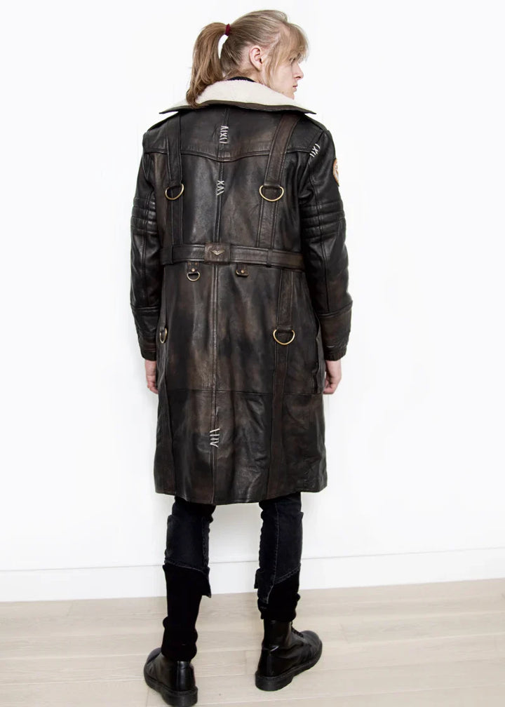 Person wearing a long dark leather coat with gold buttons on a white background