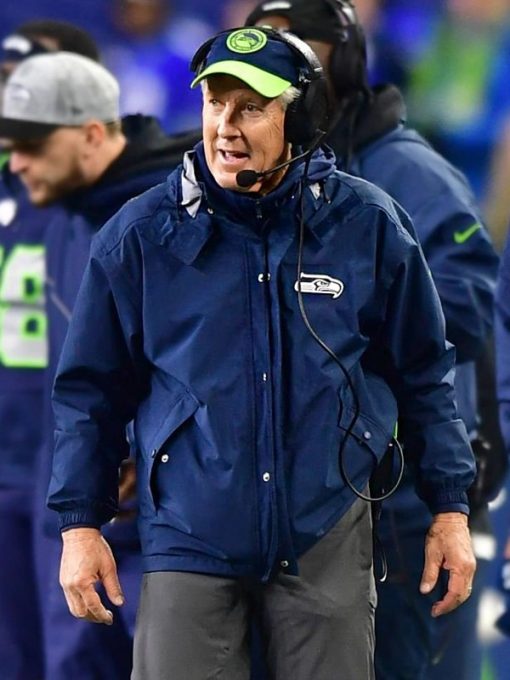 Person wearing a blue jacket with a logo, standing on a sports field.