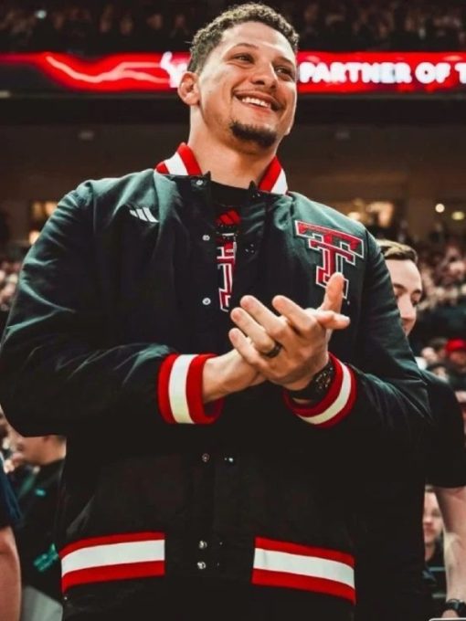 Man clapping in a sports arena wearing a dark jacket with red and white accents.