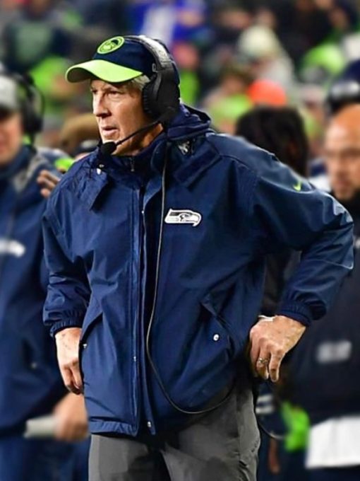 Person wearing a blue jacket with a logo, standing on a sports field.