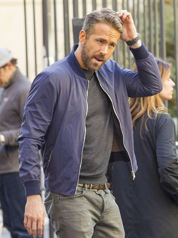 Man in a blue bomber jacket walking outdoors with people in the background