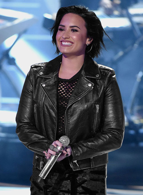 Person wearing a black leather jacket holding a microphone on a stage with blue lighting.