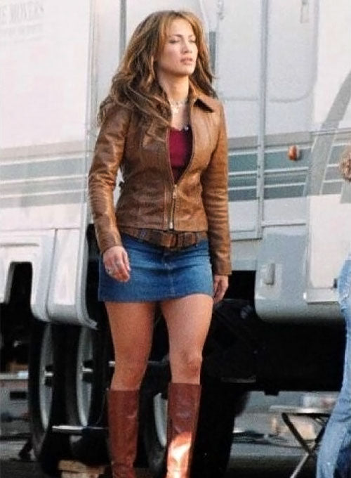 Woman wearing a brown leather jacket and blue skirt standing in front of a trailer.